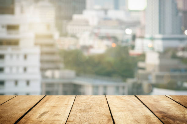 istock Panoramic empty grunge wood counter table top on blur glass window white light city bokeh background for product morning scene display montage, Abstract Blurry wide wooden desk in kitchen room rooftop. 1332346012