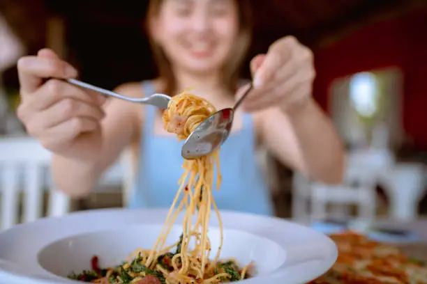 Photo of Cheerful woman eating spicy spaghetti at restaurant.