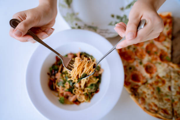 Cheerful woman eating spicy spaghetti at restaurant. Young Asian woman rolling spaghetti while eating lunch in Italian cafe. fusion food photos stock pictures, royalty-free photos & images