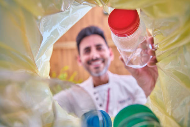 istock image from inside a recycling bin with a yellow bag of a man throwing a plastic bottle with a red cap to recycle in which his face is out of focus 1332347290