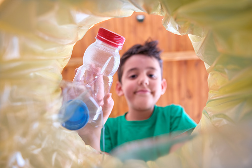 imagen desde el interior de un contenedor de reciclaje con una bolsa amarilla de un niño lanzando una botella de plástico para reciclar en la que la cara del niño está fuera de foco photo