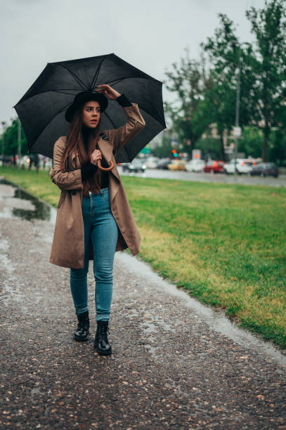黒い傘を持ち、雨の間に公園を散歩する女性 - umbrella women storm yellow ストックフォトと画像