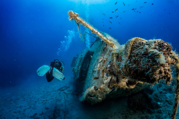 A scuba diver explores a sunken sailboat A scuba diver explores a sunken sailboat shipwreck in the ocean bottom the weaver stock pictures, royalty-free photos & images