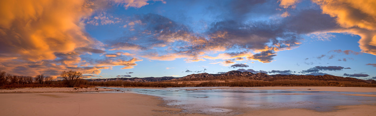 A colorful panoramic sunset view of frozen Chatfield Reservoir, with rolling hills of Front Range at horizon. Chatfield State Park, Denver-Littleton, Colorado, USA.
