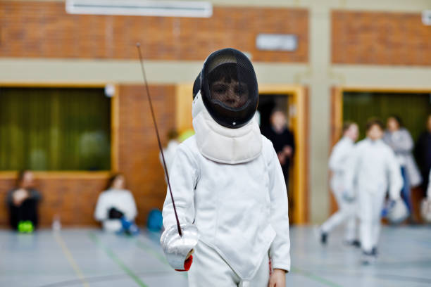 petit garçon d’escrime sur une compétition de clôture. enfant en uniforme d’escrimeur blanc avec masque et sabre. formation active des enfants avec l’enseignant et les enfants. sports et loisirs sains. - escrime photos et images de collection