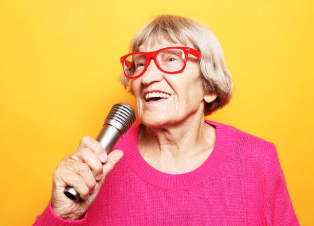 istock Happy old senior woman singing with microphone, having fun, expressing musical talent 1332358512