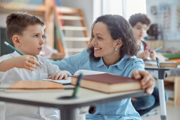 istock Happy kind teacher is helping kids in elementary school lessons 1332359740