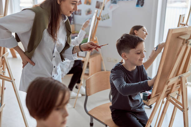 istock Young creative happy boy is drawing a picture while confident caucasian teacher helps him 1332359781