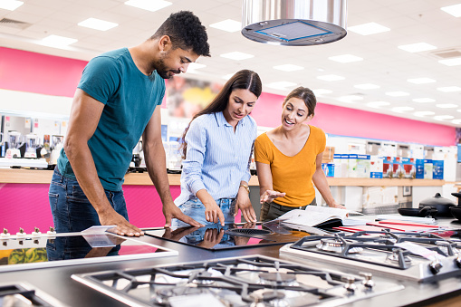 Saleswoman helps young couple choosing the best stove top for their new kitchen in a big home appliances store.