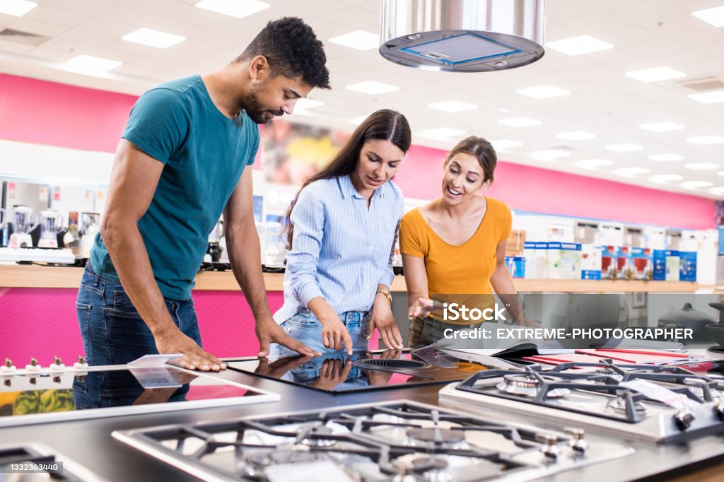 Young couple receiving assistance from a saleswoman Saleswoman helps young couple choosing the best stove top for their new kitchen in a big home appliances store. Appliance Stock Photo