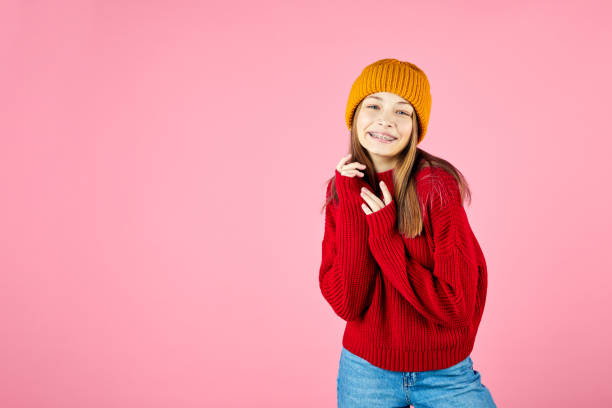 Happy young woman wearing warm sweater and knitted hat on pink background. Girl winter portrait. Smiling hipster with braces having fun. Happy young woman wearing warm sweater and knitted hat on pink background. Smiling hipster with braces having fun. kids winter fashion stock pictures, royalty-free photos & images