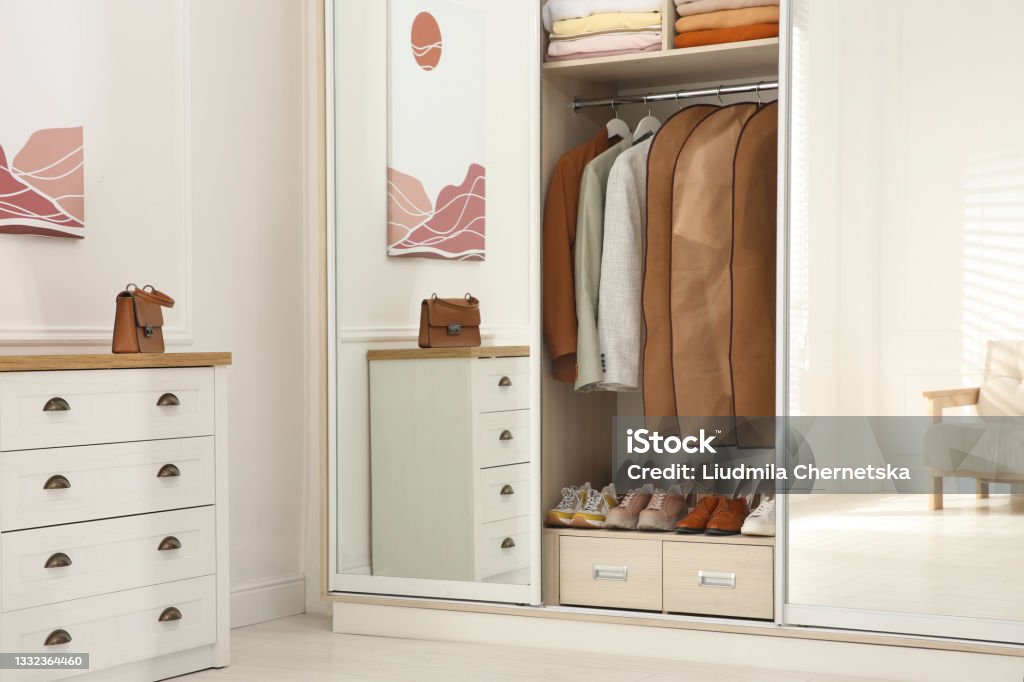 Garment bags with clothes on rack in wardrobe indoors Closet Stock Photo