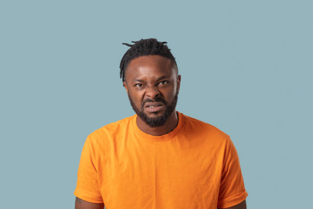 very angry dreadlock young man with grimace in orange t-shirt , blue background stock photo