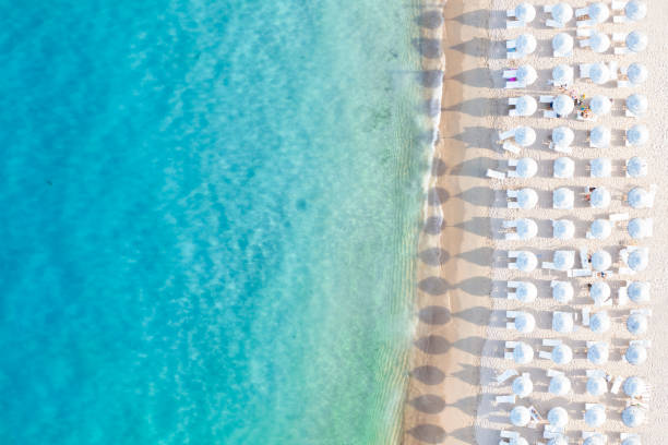 View from above, stunning aerial view of a white sand beach bathed by a turquoise water and relaxed people under some beach umbrellas at sunset. Cala di volpe beach, Costa Smeralda, Sardinia, Italy. View from above, stunning aerial view of a white sand beach bathed by a turquoise water and relaxed people under some beach umbrellas at sunset. Cala di volpe beach, Costa Smeralda, Sardinia, Italy. Cala Di Volpe stock pictures, royalty-free photos & images