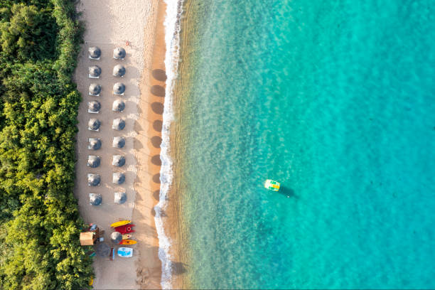 View from above, stunning aerial view of a beautiful  beach bathed by a turquoise water and some beach umbrellas illuminated at sunset. Cala di volpe beach, Costa Smeralda, Sardinia, Italy. View from above, stunning aerial view of a beautiful  beach bathed by a turquoise water and some beach umbrellas illuminated at sunset. Cala di volpe beach, Costa Smeralda, Sardinia, Italy. Cala Di Volpe stock pictures, royalty-free photos & images