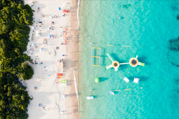 View from above, stunning aerial view of a white sand beach bathed by a turquoise water and relaxed people under some beach umbrellas at sunset. Cala di volpe beach, Costa Smeralda, Sardinia, Italy. View from above, stunning aerial view of a white sand beach bathed by a turquoise water and relaxed people under some beach umbrellas at sunset. Cala di volpe beach, Costa Smeralda, Sardinia, Italy. Cala Di Volpe stock pictures, royalty-free photos & images
