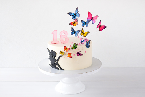 White birthday cake for girls, decorated with a silhouette of a fairy and colorful butterflies.