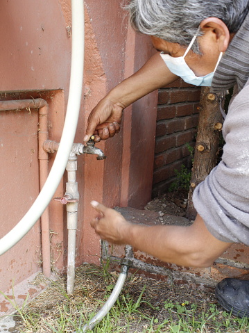 adult man checking a water tap in a garden and wearing a mask