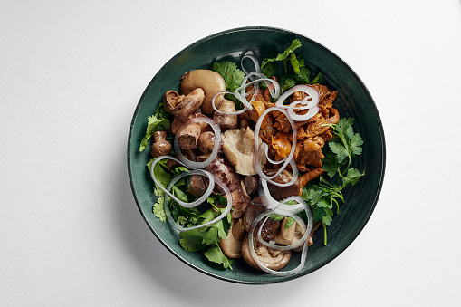 Mushrooms with onions and herbs, assorted pickled mushrooms in a plate on a light background, top view, copy space light background.