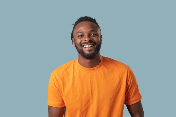 Very happy young man man Studio portrait of handsome dreadlock man in orange shirt smiling in front of blue background ecstatic photos stock pictures, royalty-free photos & images