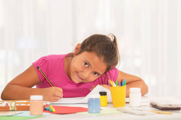 istock Smiling little girl drawing and looking at camera in class 1332375145