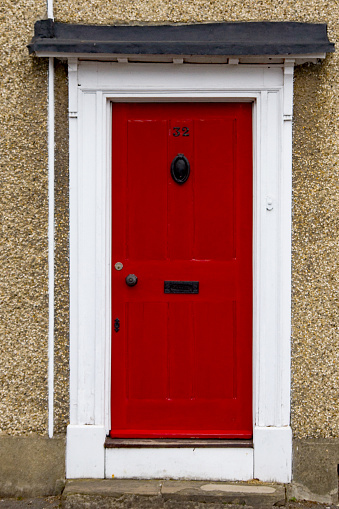 The house number 32 on a red wooden painted front door frame in Hertfordshire, with a brass door knocker, And letter box with handle