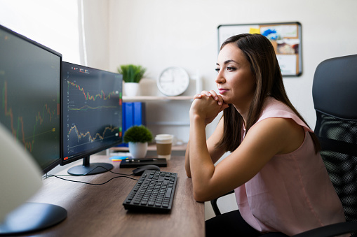 Freelance young woman working as a broker at home and looking at the computer monitor while checking the stock market