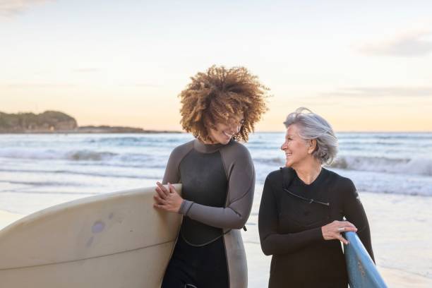 une femme heureuse à la retraite prend des cours de surf - exercising wetsuit people expressing positivity photos et images de collection