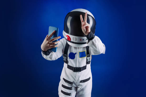 Teenager wearing astronaut costume and helmet using smartphone Teenager wearing astronaut costume and helmet using smartphone for messaging or taking selfie standing on dark blue background with copy space. cosmonaut photos stock pictures, royalty-free photos & images