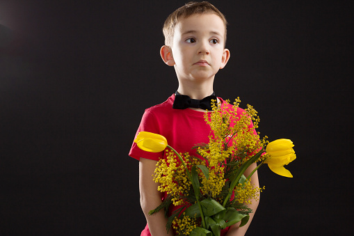 a boy with vitiligo in a red T-shirt with a bouquet of mimosa on a black studio background