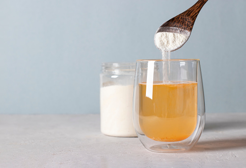 El colágeno en polvo se agrega al vaso de agua con una cuchara. Concepto saludable y anti-edad sobre fondo azul claro. Espacio de copia photo