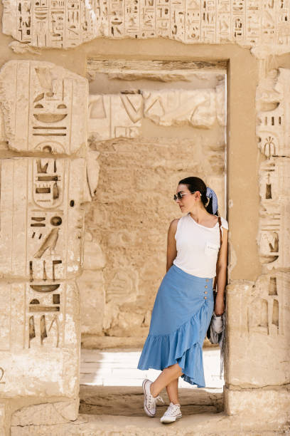 istock Stylish female traveler standing in between stone construction and admiring historic architecture in ancient ruined heritage building with hieroglyphs on weathered columns 1332389310
