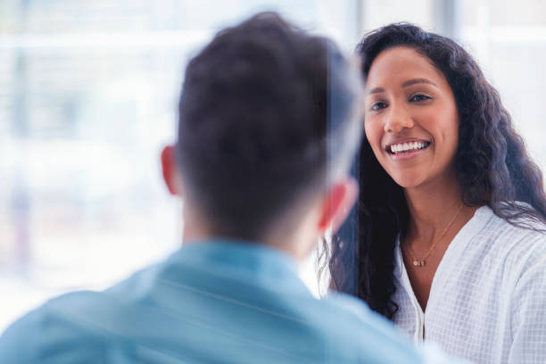 Business colleagues having a conversation. Business colleagues having a conversation. They are both young business people casually dressed in a bright office. Could be an interview or consultant working with a client. She is listening carefully. One person has his back to us casual job interview stock pictures, royalty-free photos & images