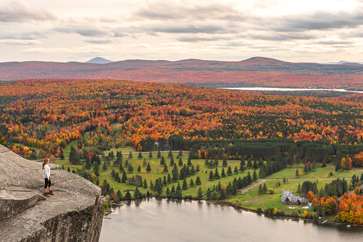 Woman looking at Lyster lake with forest of Quebec and Vermont seen from the Mount Pinacle in Coaticook during autumn.