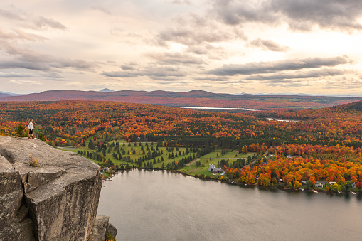 Woman looking at Lyster lake with forest of Quebec and Vermont seen from the Mount Pinacle in Coaticook during autumn.