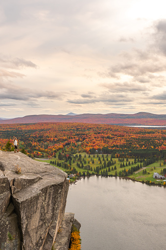 Woman looking at Lyster lake with forest of Quebec and Vermont seen from the Mount Pinacle in Coaticook during autumn.