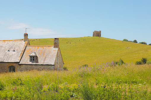 An old stone cottage and a distant St Catherine's Chapel  in the quaint rural countryside at the village of Abbotsbury on a sunny summer day in Dorset, England, UK.