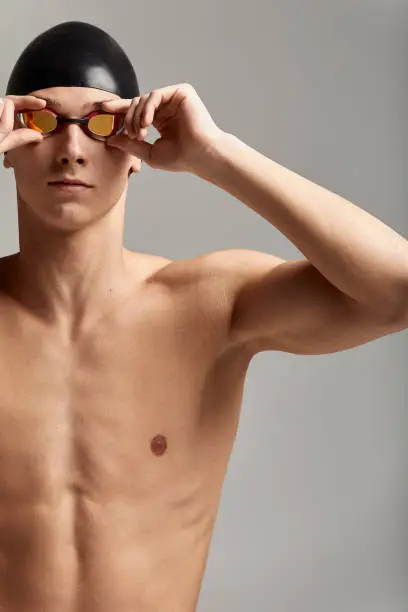 Photo of Young male swimmer preparing for the start, close-up portrait of a swimmer in a mask and a hat, gray background, copy space, swimming concept