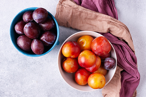 Blue and pink plums plums in a round plate and a blue and pink napkin on a white background.