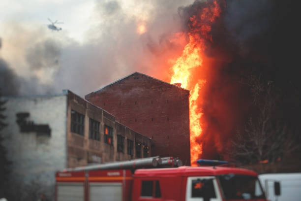 Massive large blaze fire in the city, brick factory building on fire, hell major fire explosion flame blast,  with firefighters team firemen on duty, arson, burning house damage destruction stock photo