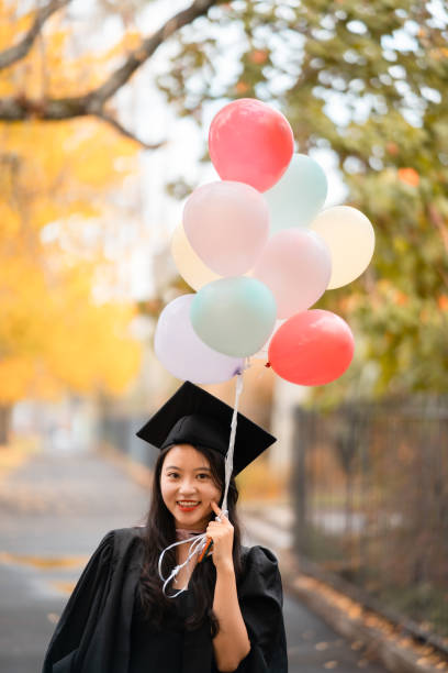 mujer graduada sosteniendo globos. - graduation student women beauty fotografías e imágenes de stock