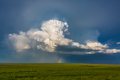Double rainbow under developing thunderhead (cumulonimbus) storm clouds forming over green fields in Montana: exploding upward, majestic power