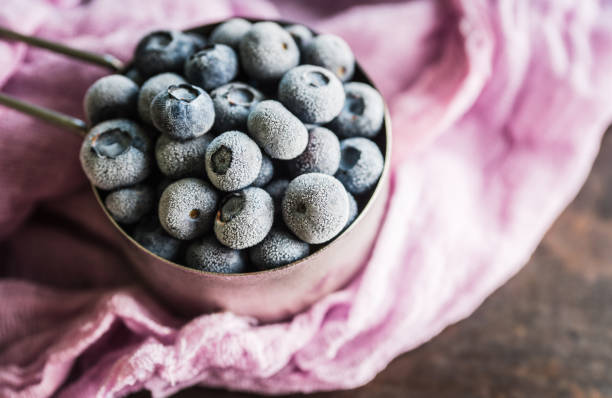 Frozen blueberries in metal cup on the rustic background. Selective focus.