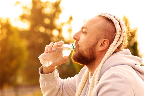 istock In the morning at sunrise, a man with an interesting braid hairstyle drinks water from a bottle after a workout 1332427741