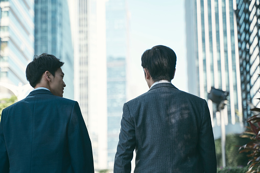 rear view of two asian corporate businessmen walking talking in central business district in modern city