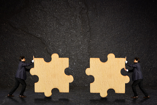 Two businessman working together in tandem to put up two puzzle pieces in order to succeed. puzzle pieces rendered by computer graphic.