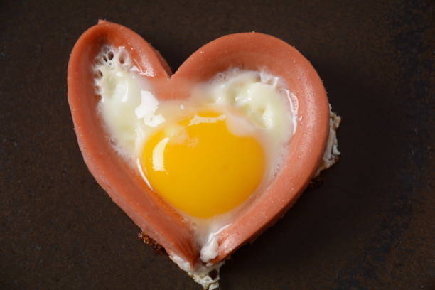 istock Two sausages in a heart-shaped fried eggs on black plate. Breakfast on Valentine's Day 1332440615