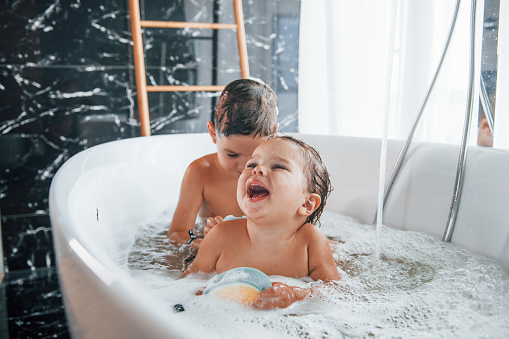 Dos niños divirtiéndose y lavándose en el baño en casa. Ayudándose unos a otros photo