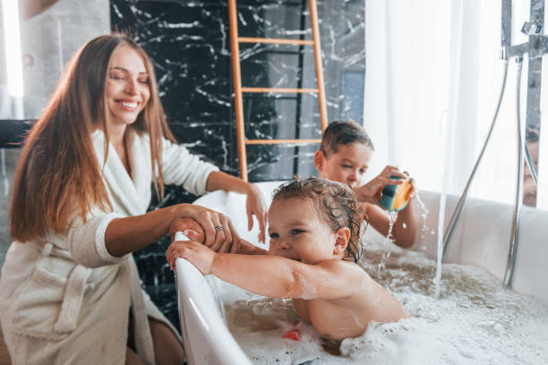Young mother helps her son and daughter. Two kids washing in the bath Young mother helps her son and daughter. Two kids washing in the bath. taking a bath photos stock pictures, royalty-free photos & images