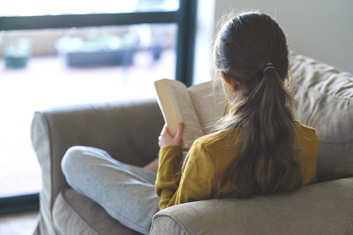 Long hair girl is reading a book next to the window.